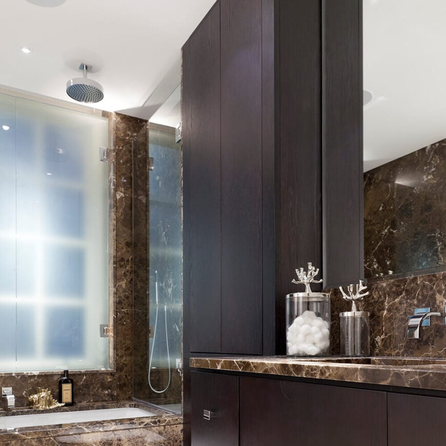 这间浴室拥有较深的色调，深大理石色调和深色染色木橱柜。浴缸，台面，甚至墙壁都与丰富的大理石齐平，使一个豪华的约会。