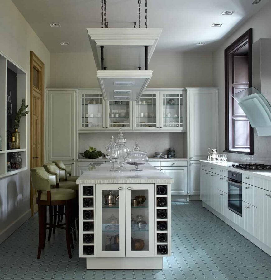 这个传统的厨房有淡绿色图案的地砖，与白色的木制摇床柜和抽屉形成对比，这些橱柜和抽屉与白色的墙壁和天花板融为一体，天花板上悬挂着一个架子。
