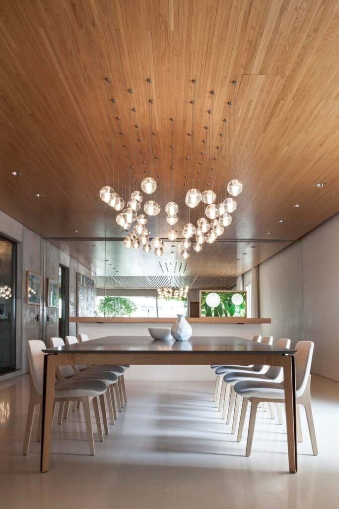 餐厅拥有一个木质天花板，配有嵌入式照明和气泡玻璃吊坠，悬挂在木桌和白色椅子上。