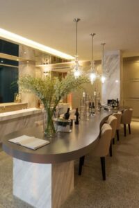 时尚的餐厅展示了米色的椅子和灰色的弧形餐桌，固定在大理石柱子上，天花板上悬挂着玻璃吊坠。