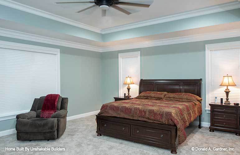 主卧室有地毯地板，柔和的绿色墙壁和装有风扇的托盘天花板。