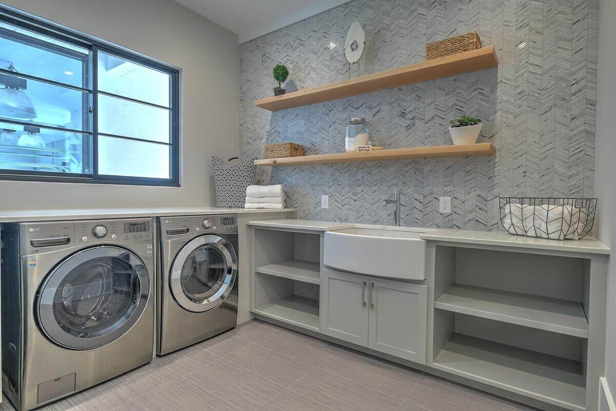 洗衣房，内置架子，洗衣机和烘干机，多个柜台，和一个实用水槽顶部有木制浮动架子。