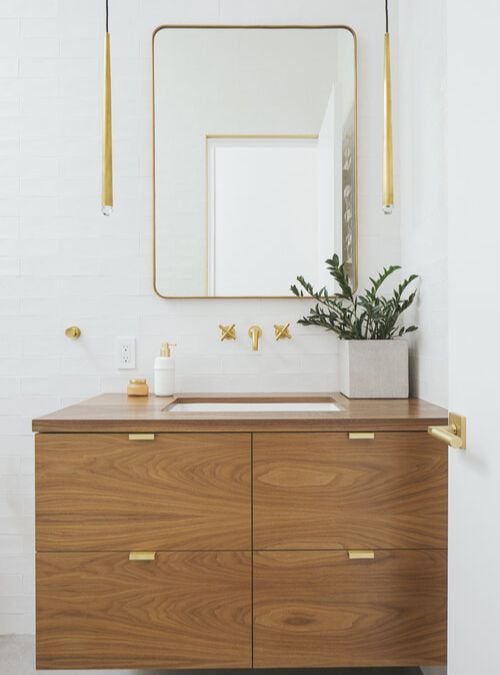 盥洗室的室内照片,展示一个水槽伴随橱柜,固定在墙上的镜子为焦点,强调优雅的室内设计以木质和黄金颜色主题。